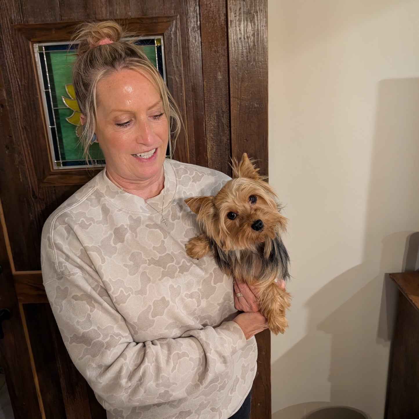 Woman holding a small dog in a room with wooden walls and a door.
